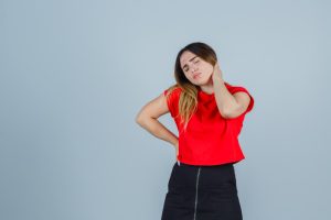 Woman holding her neck in pain against a gray background, expressing discomfort and tension